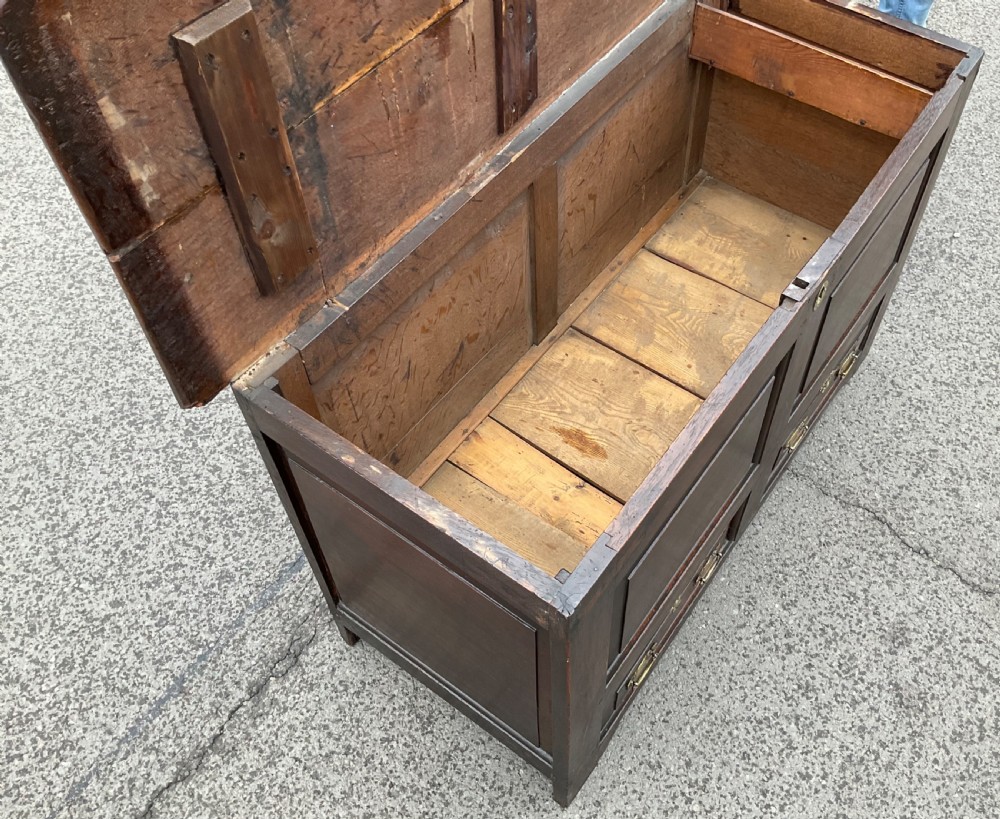 An antique dark oak mule chest featuring two raised front panels above two short drawers with brass handles and keyholes. View VI