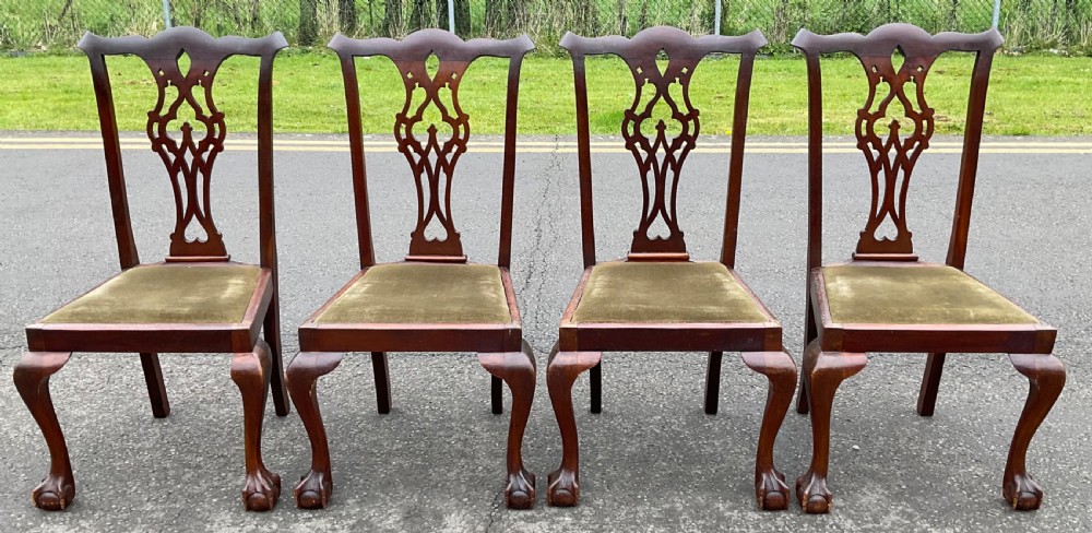 A set of four Chippendale style mahogany dining chairs with carved pierced back splats, olive fabric drop-in seats, and cabriole front legs ending in ball and claw feet.