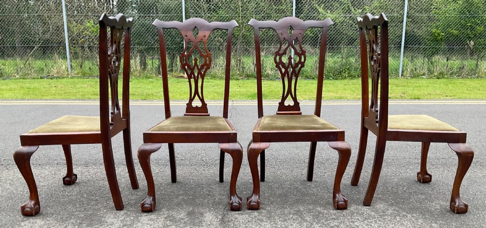 A set of four Chippendale style mahogany dining chairs with carved pierced back splats, olive fabric drop-in seats, and cabriole front legs ending in ball and claw feet. View V
