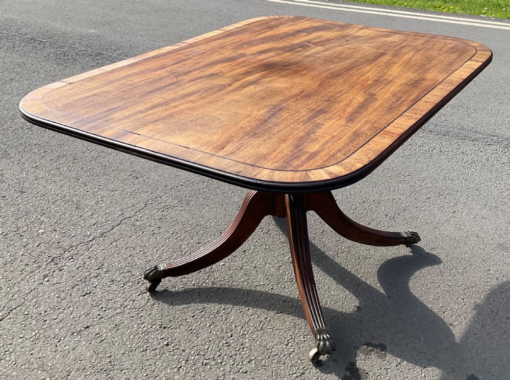 A Georgian mahogany tilt-top breakfast table featuring a crossbanded border, fine inlay stringing, and reeded quadruped legs ending in brass claw feet with castors. View VII