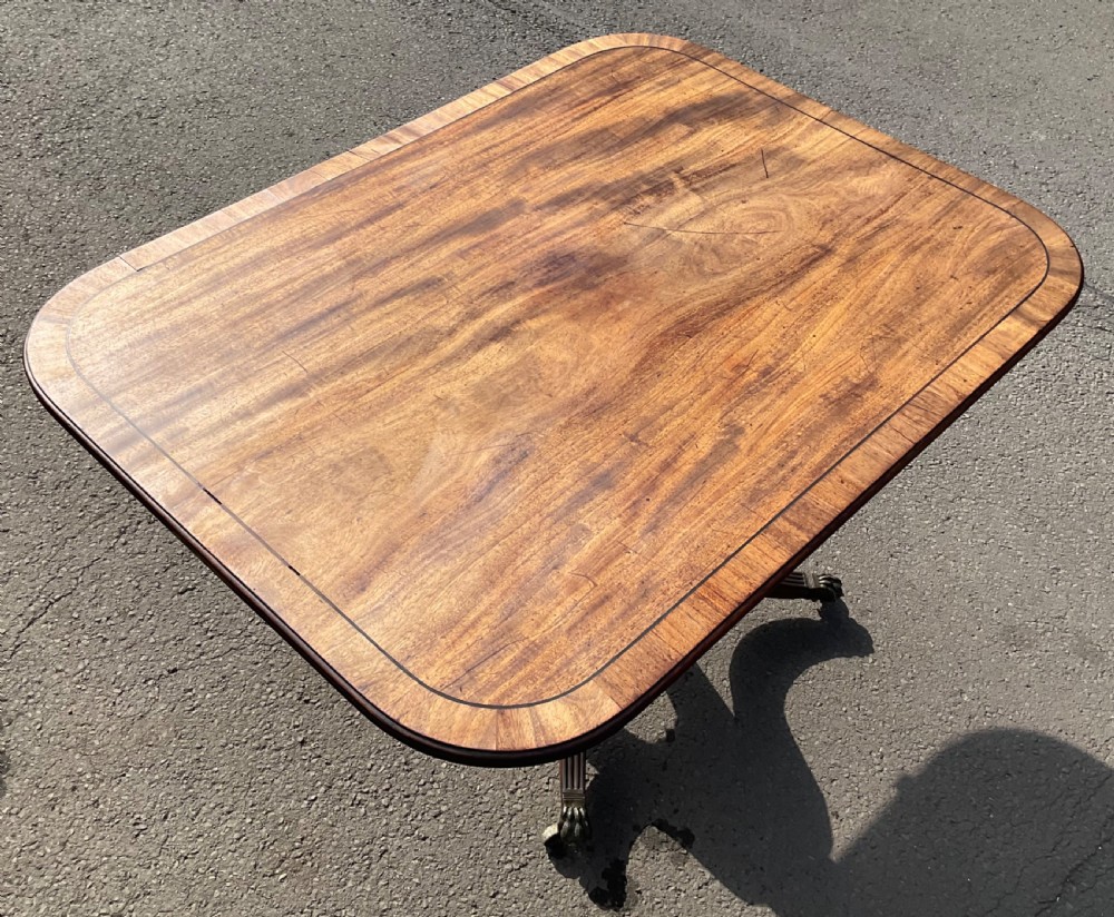 A Georgian mahogany tilt-top breakfast table featuring a crossbanded border, fine inlay stringing, and reeded quadruped legs ending in brass claw feet with castors. View X