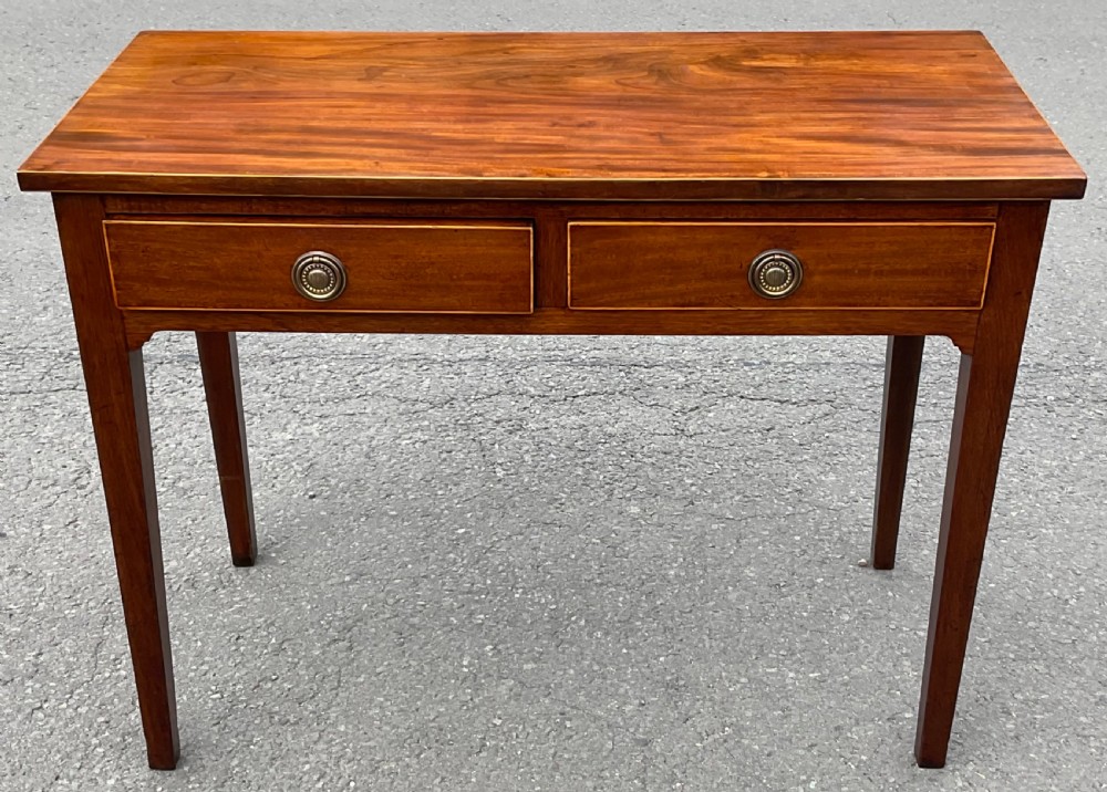 A Georgian mahogany side table featuring two drawers with brass ring handles and straight tapered legs.