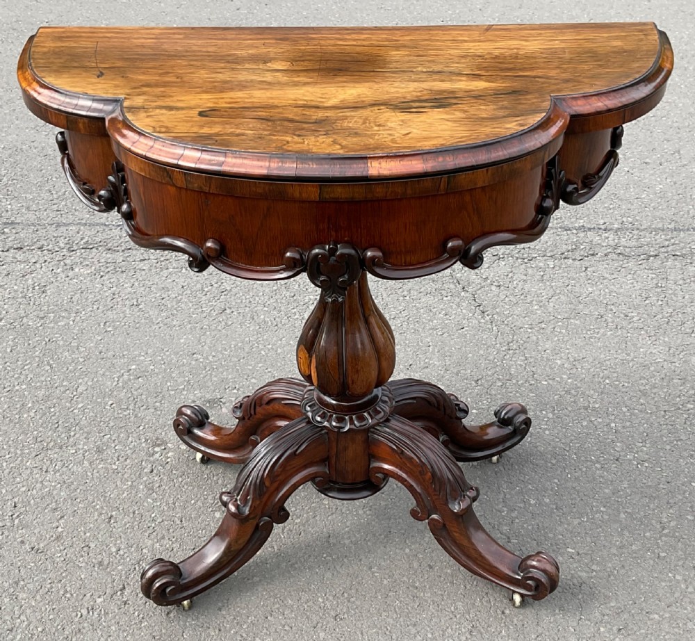 A Victorian rosewood fold-over card table featuring a shaped carved apron, bulbous turned pedestal, and four scrolled legs with brass castors. View II