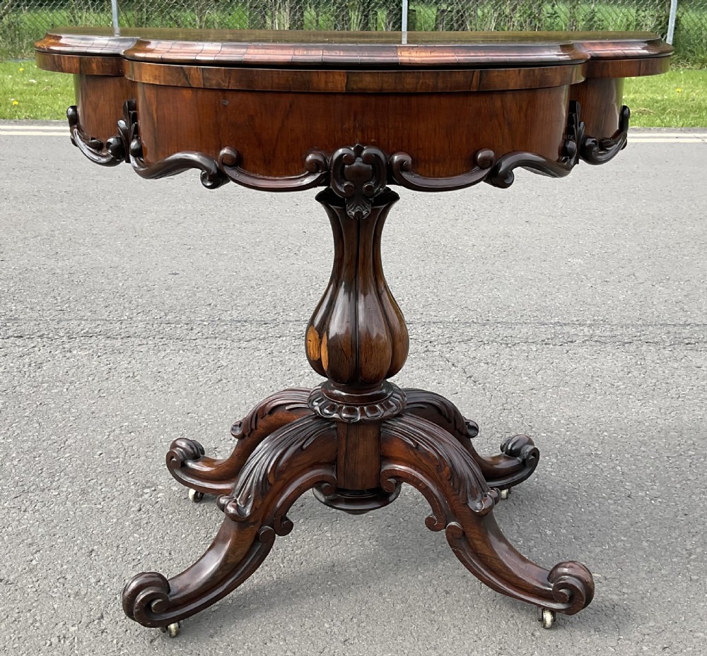 A Victorian rosewood fold-over card table featuring a shaped carved apron, bulbous turned pedestal, and four scrolled legs with brass castors. View III