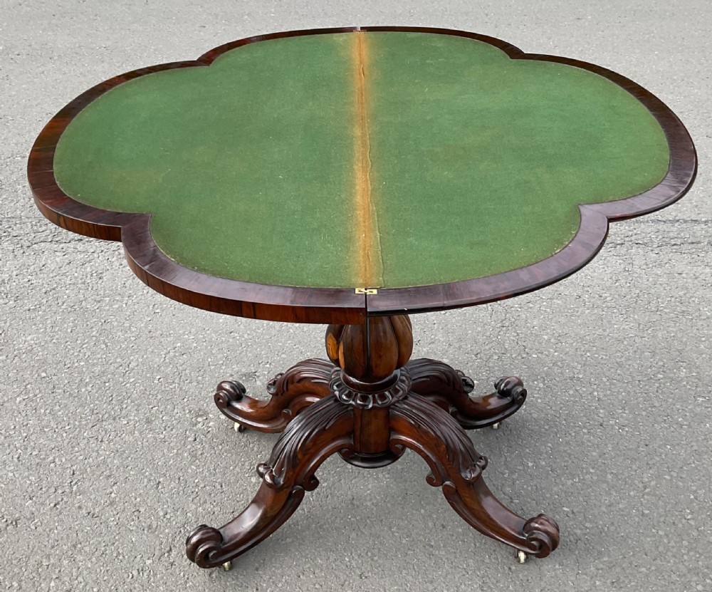 A Victorian rosewood fold-over card table featuring a shaped carved apron, bulbous turned pedestal, and four scrolled legs with brass castors. View IX