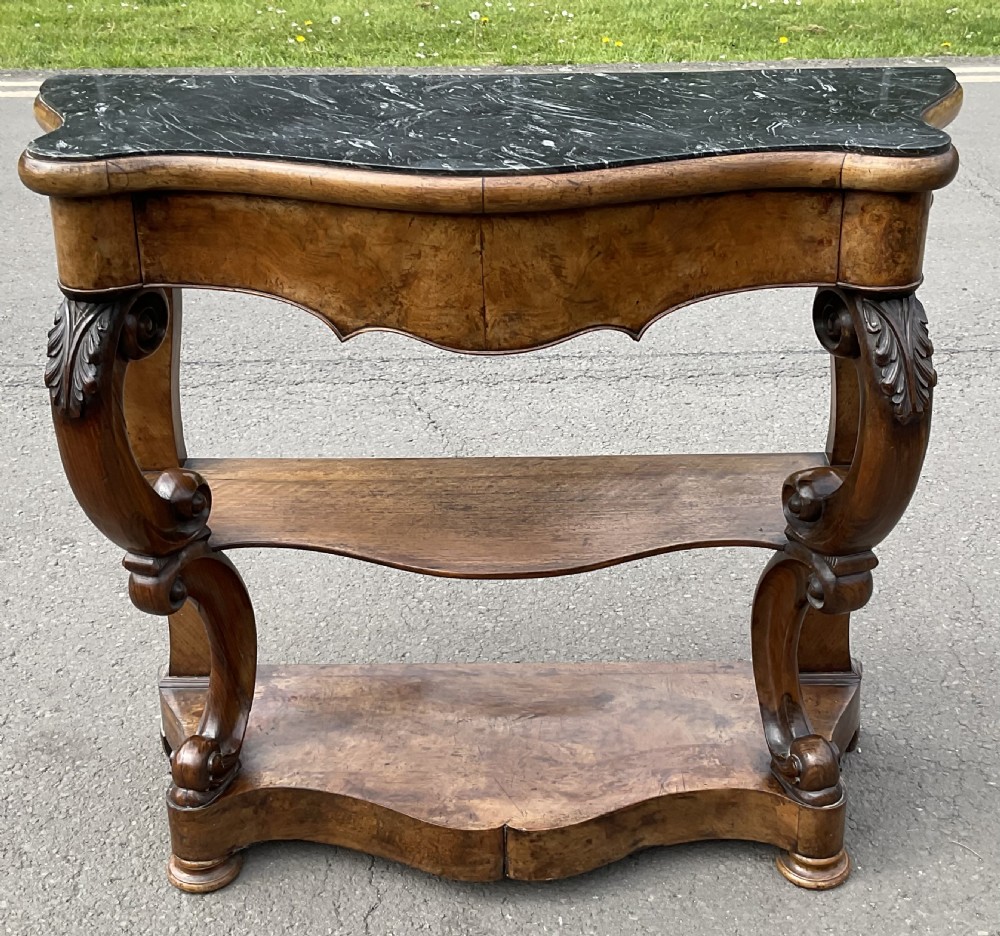 A Victorian serpentine-front console table crafted from figured wood with a dark green marble top and carved scroll legs.
