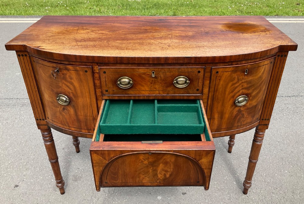 A Georgian bowfront mahogany sideboard featuring turned legs, brass oval drop handles, stringing inlay, and fluted corner pilasters. View VI