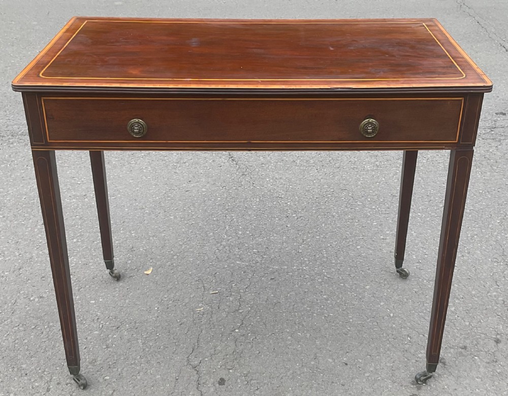A Georgian mahogany writing table featuring boxwood string inlay on the rectangular top, a single drawer with twin brass ring handles, and square tapered legs on brass castors.