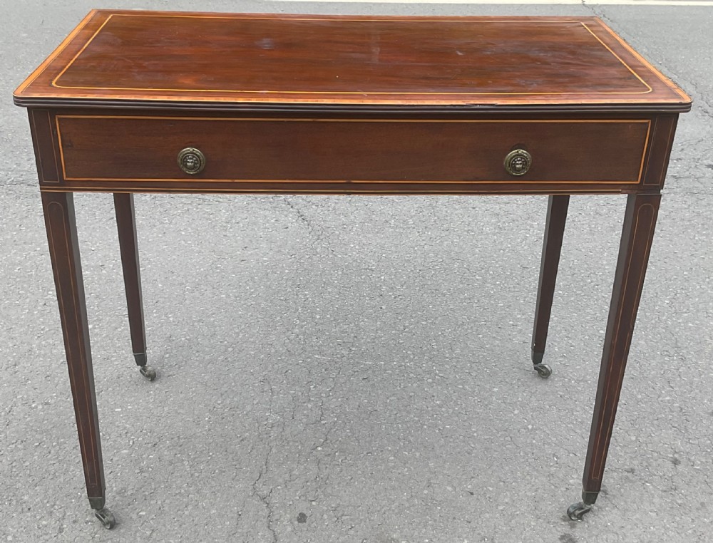 A Georgian mahogany writing table featuring boxwood string inlay on the rectangular top, a single drawer with twin brass ring handles, and square tapered legs on brass castors. View II