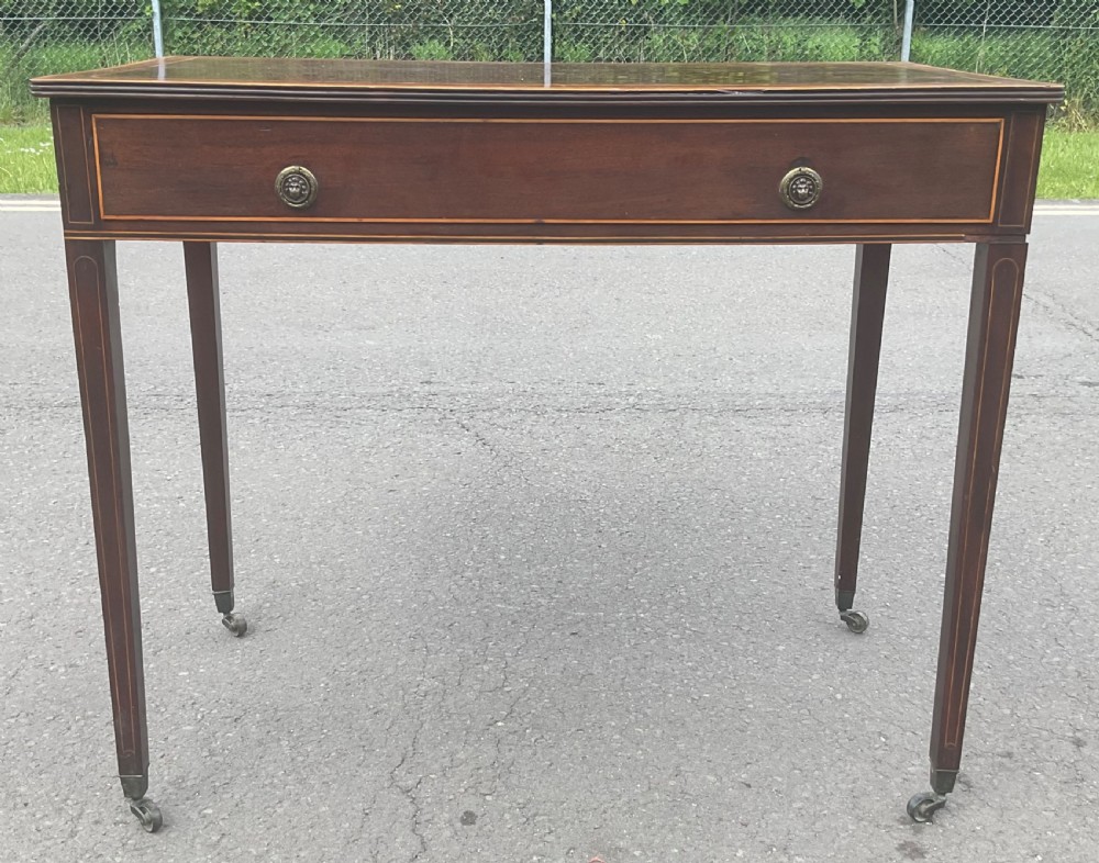 A Georgian mahogany writing table featuring boxwood string inlay on the rectangular top, a single drawer with twin brass ring handles, and square tapered legs on brass castors. View V