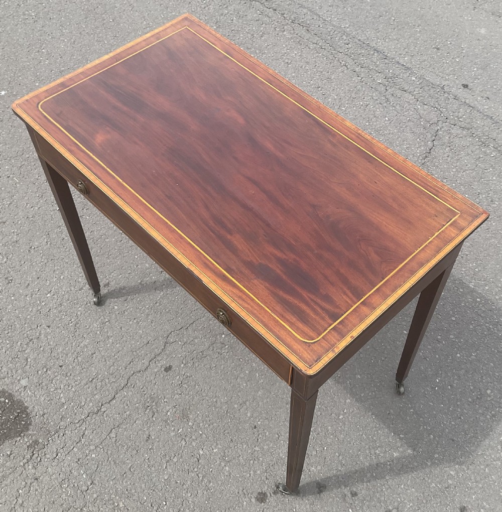 A Georgian mahogany writing table featuring boxwood string inlay on the rectangular top, a single drawer with twin brass ring handles, and square tapered legs on brass castors. View VI