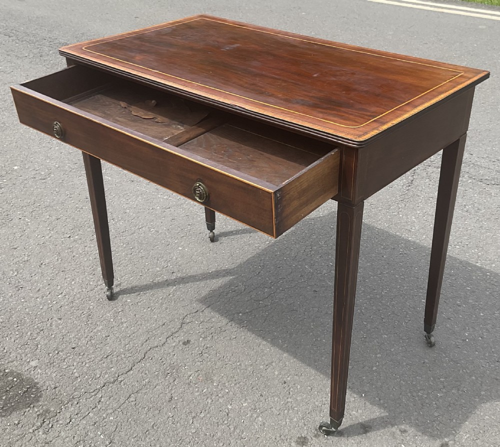 A Georgian mahogany writing table featuring boxwood string inlay on the rectangular top, a single drawer with twin brass ring handles, and square tapered legs on brass castors. View X