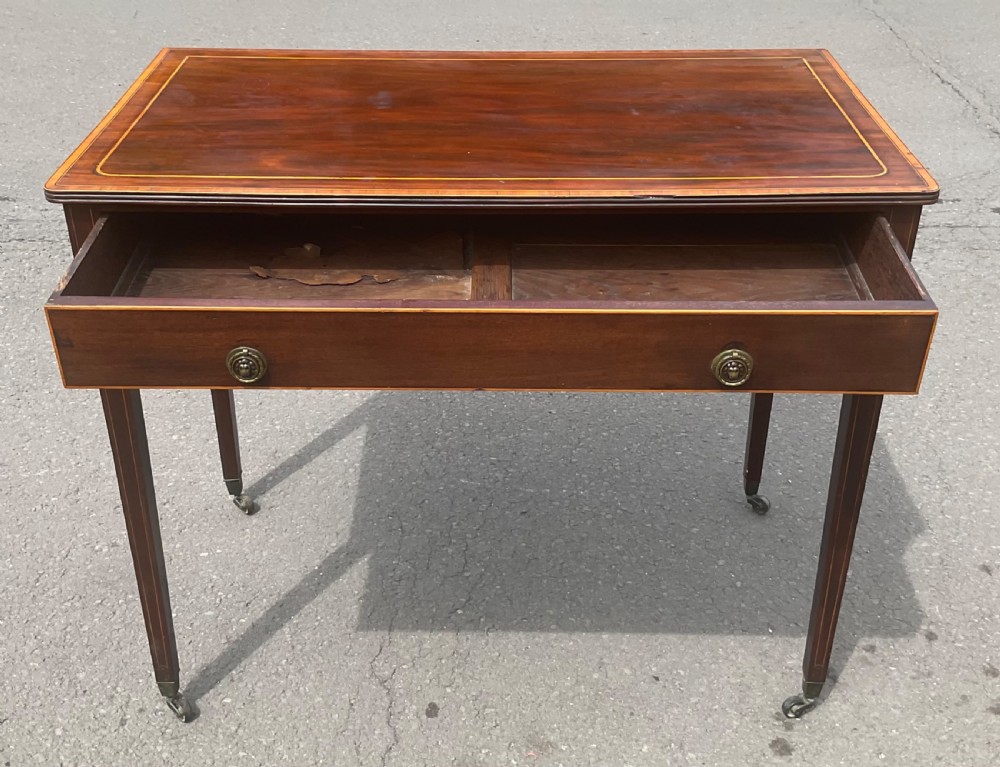 A Georgian mahogany writing table featuring boxwood string inlay on the rectangular top, a single drawer with twin brass ring handles, and square tapered legs on brass castors. View XI