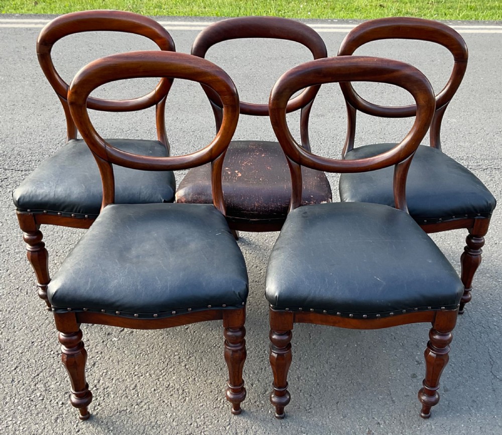 A set of five Victorian mahogany dining chairs featuring rounded balloon backrests, dark leather upholstered seats, and turned front legs. View IV