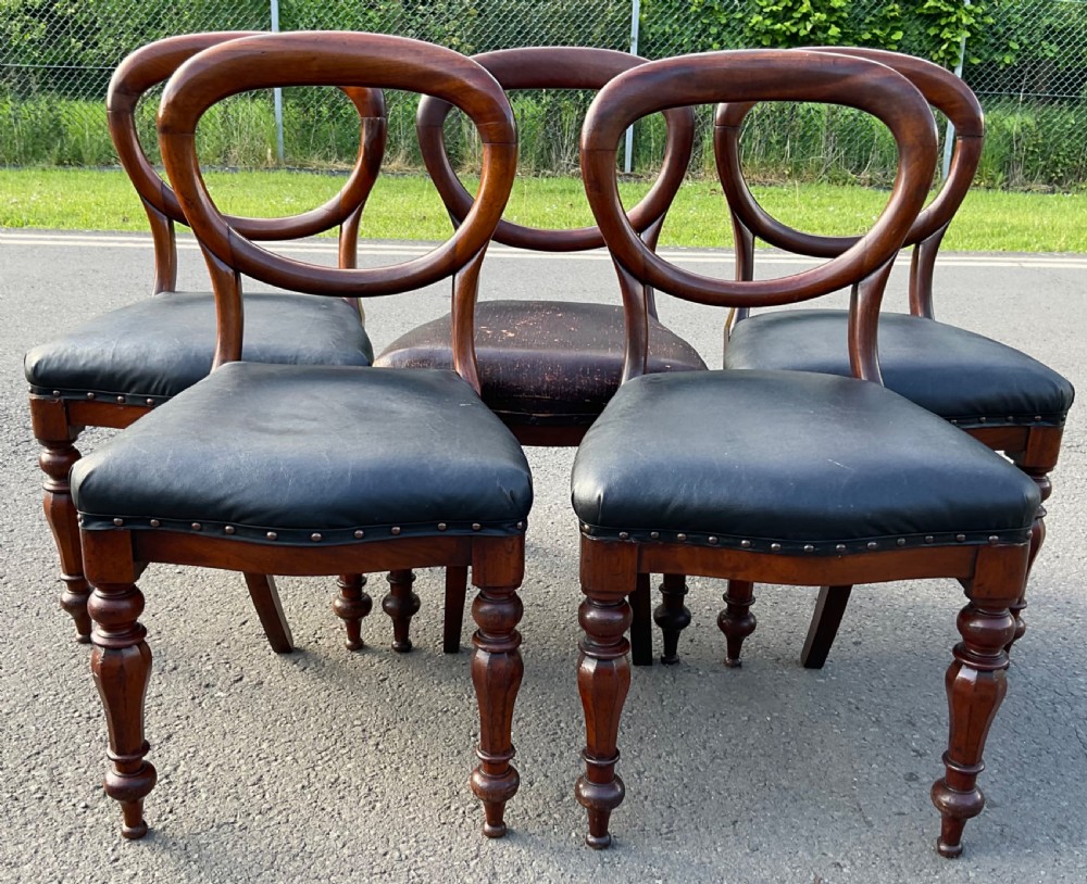 A set of five Victorian mahogany dining chairs featuring rounded balloon backrests, dark leather upholstered seats, and turned front legs. View V