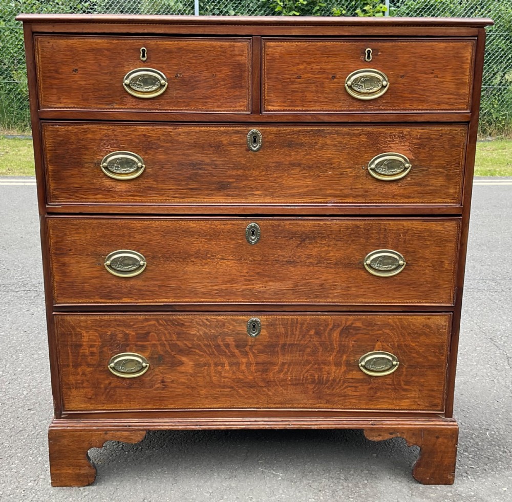 A Georgian oak chest of drawers featuring a two-over-three drawer configuration with oval brass drop handles and bracket feet. View II