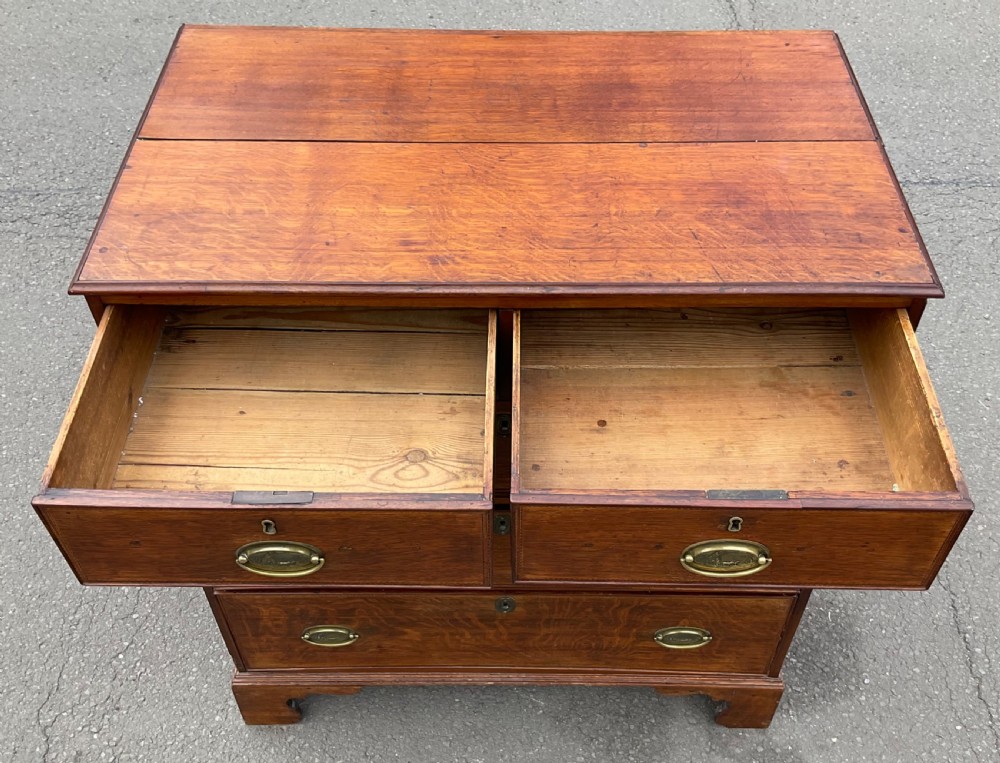 A Georgian oak chest of drawers featuring a two-over-three drawer configuration with oval brass drop handles and bracket feet. View X