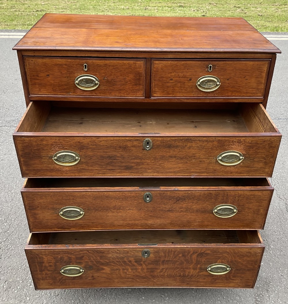 A Georgian oak chest of drawers featuring a two-over-three drawer configuration with oval brass drop handles and bracket feet. View XI