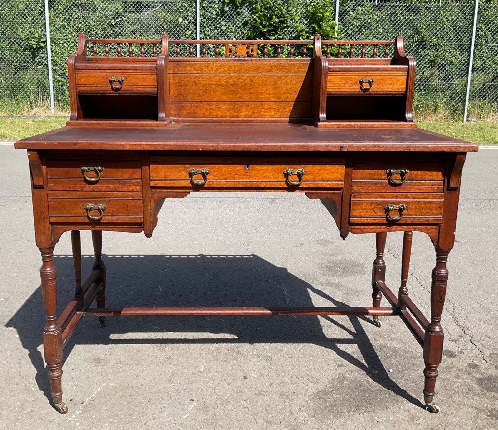 An Edwardian walnut kneehole writing desk with a leather inset top, brass ring handles, turned legs, and a raised drawer gallery.