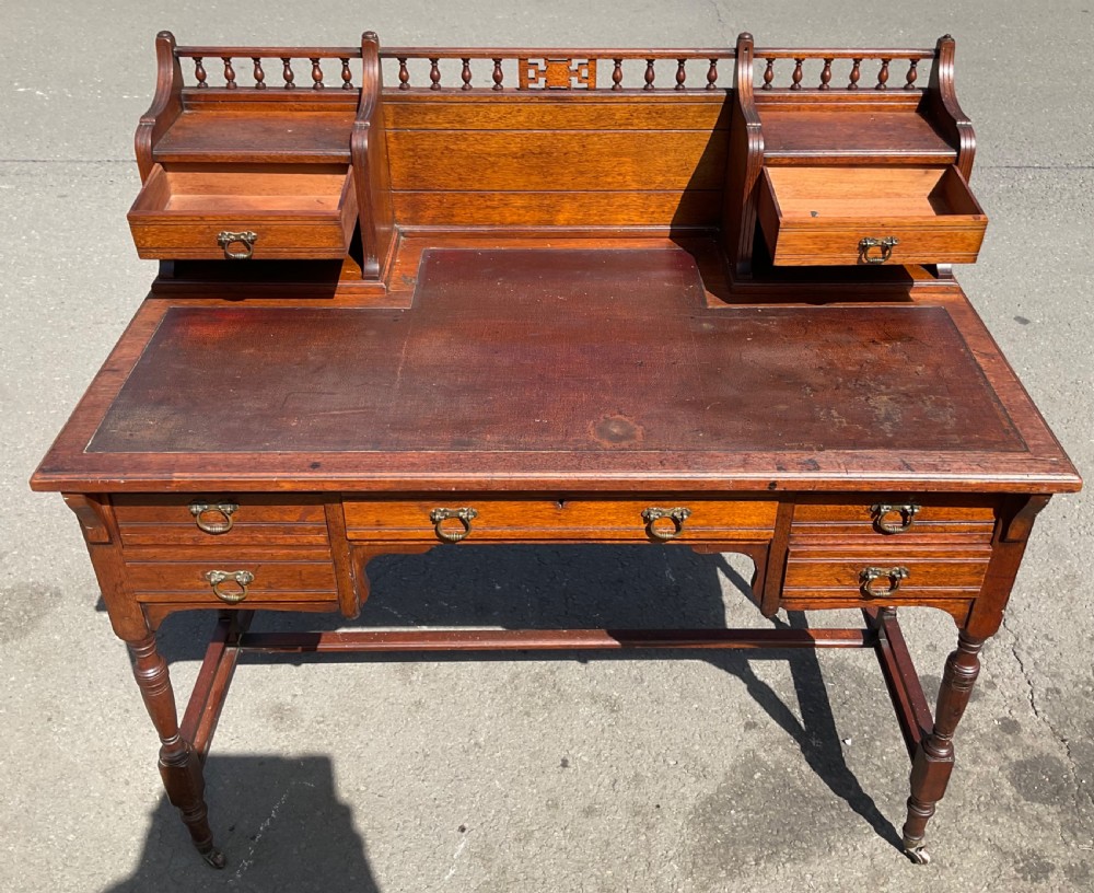 An Edwardian walnut kneehole writing desk with a leather inset top, brass ring handles, turned legs, and a raised drawer gallery. View VII