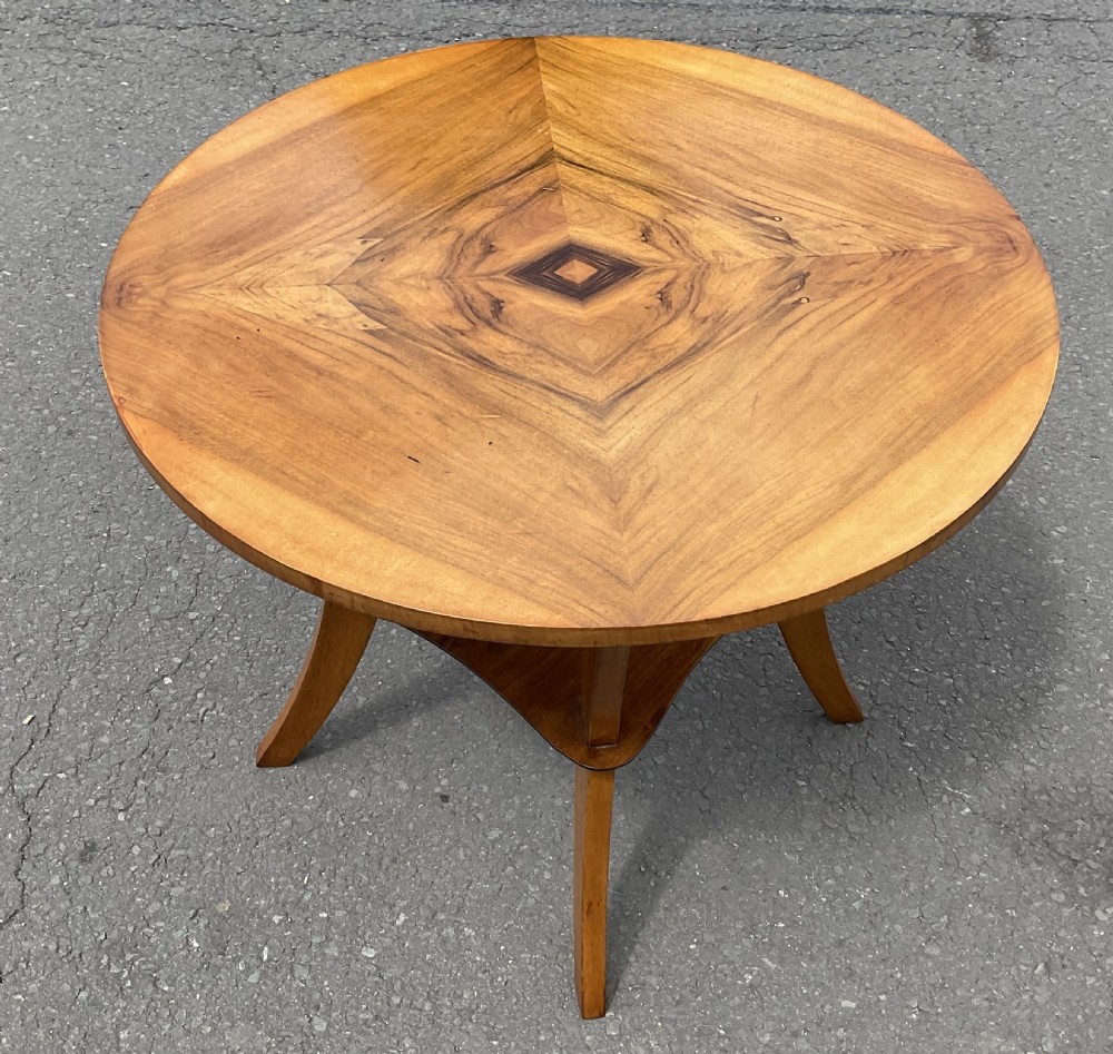 An Art Deco circular walnut centre table featuring a diamond bookmatched veneered top, four swept legs, and a shaped lower tier. View II