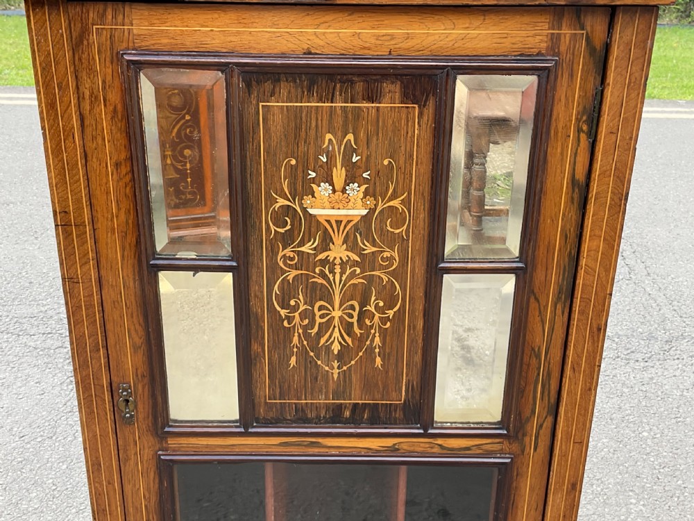 An Edwardian inlaid rosewood music cabinet featuring marquetry urn motifs, mirrored panels, a glazed lower door, and turned corner finials. View V
