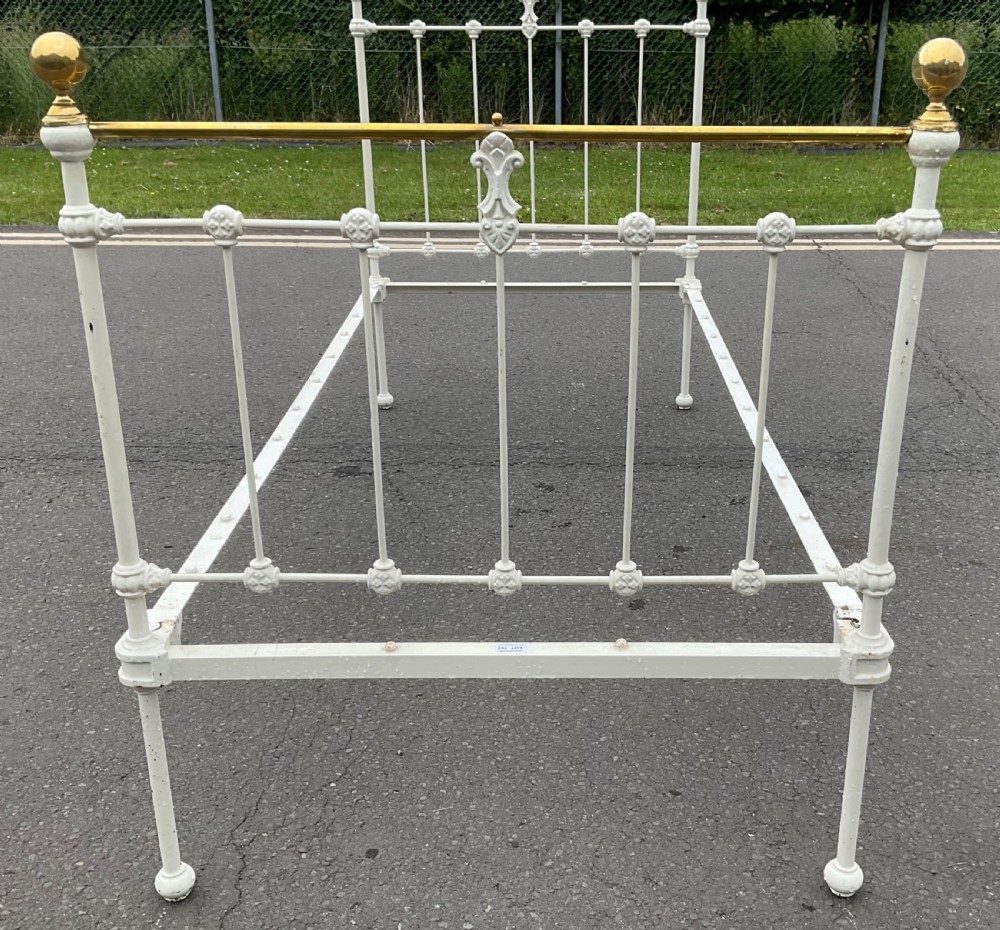 An off-white painted cast iron single bed frame featuring vertical spindles, decorative cast rosettes, central fleur-de-lis motifs, polished brass top rails, and brass spherical finials. View VIII