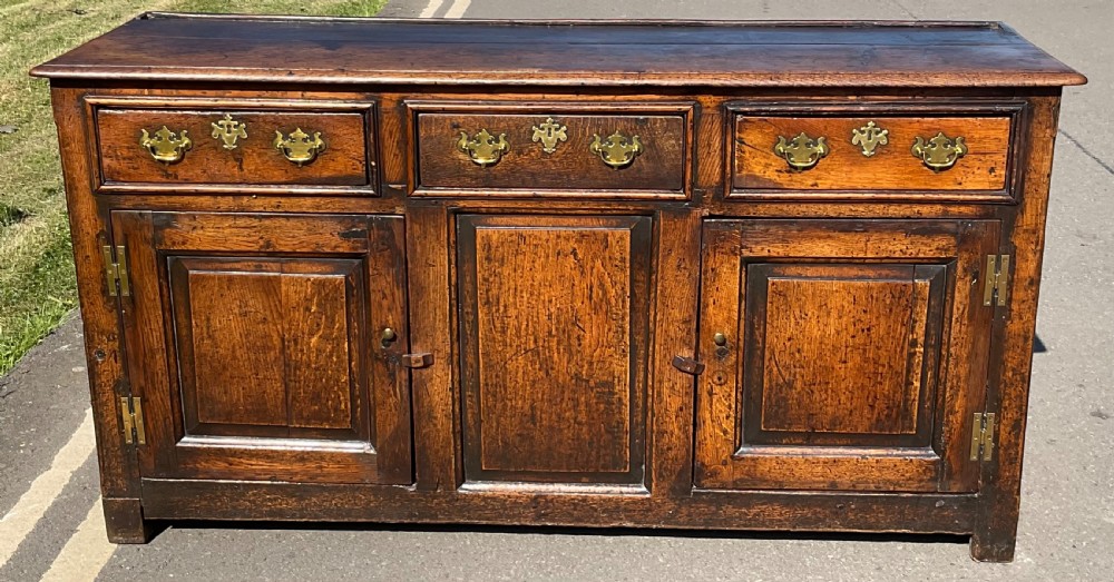 A Georgian period oak dresser base featuring three top drawers with brass handles above three cupboard doors with fielded panels.