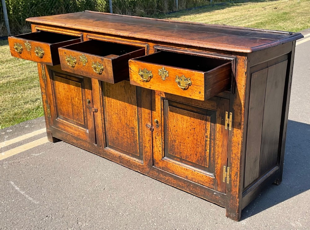 A Georgian period oak dresser base featuring three top drawers with brass handles above three cupboard doors with fielded panels. View III