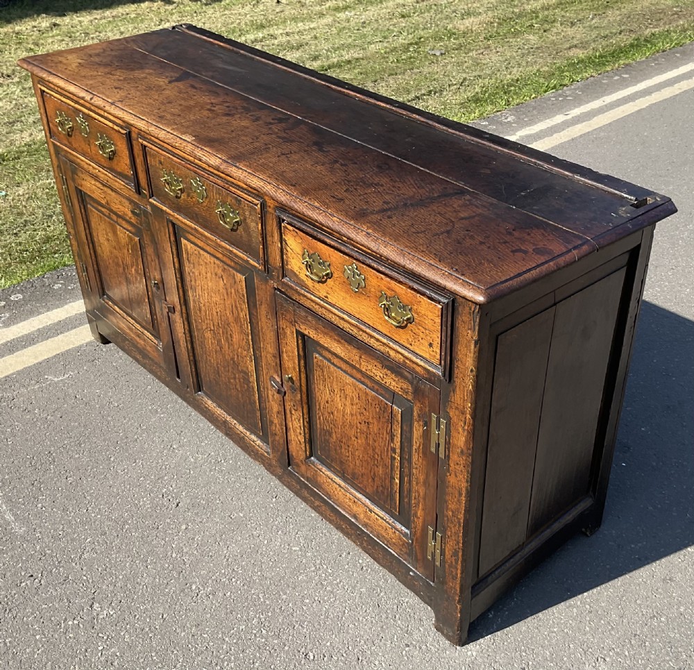 A Georgian period oak dresser base featuring three top drawers with brass handles above three cupboard doors with fielded panels. View IV
