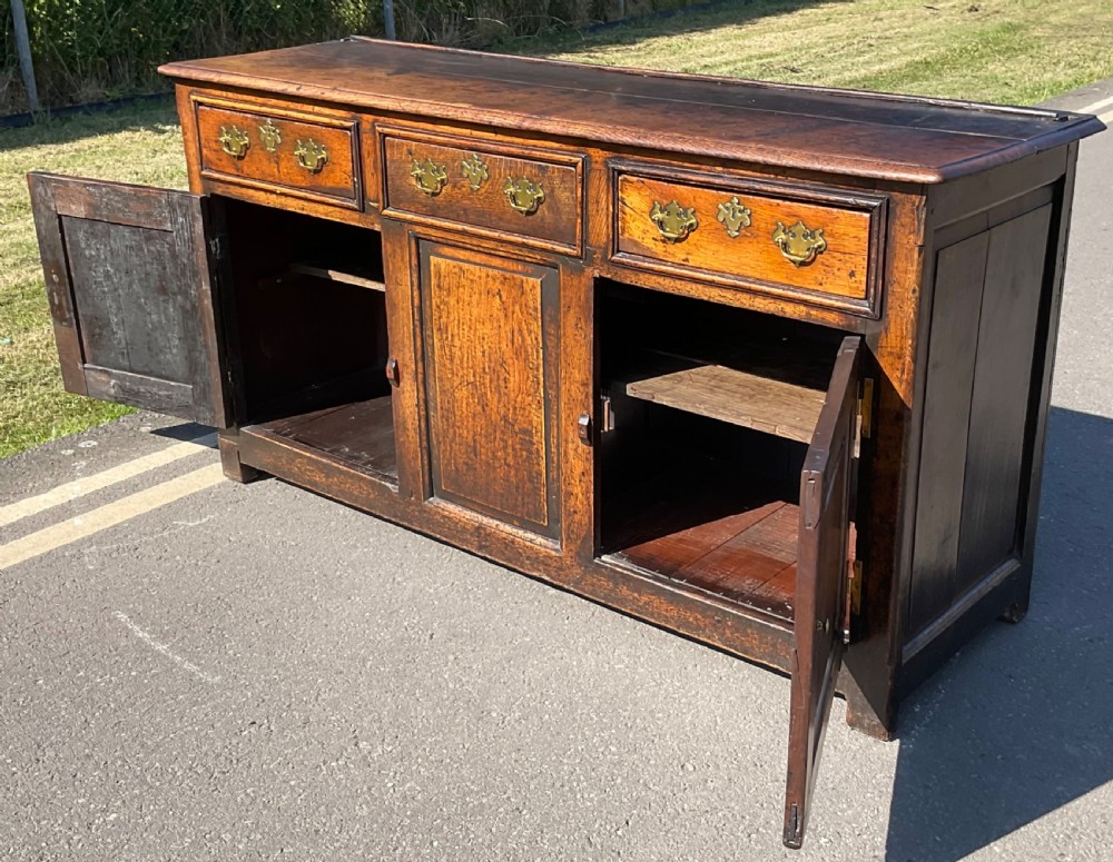 A Georgian period oak dresser base featuring three top drawers with brass handles above three cupboard doors with fielded panels. View V