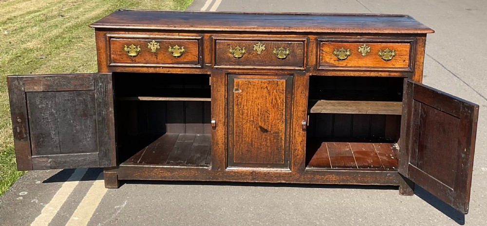 A Georgian period oak dresser base featuring three top drawers with brass handles above three cupboard doors with fielded panels. View VI