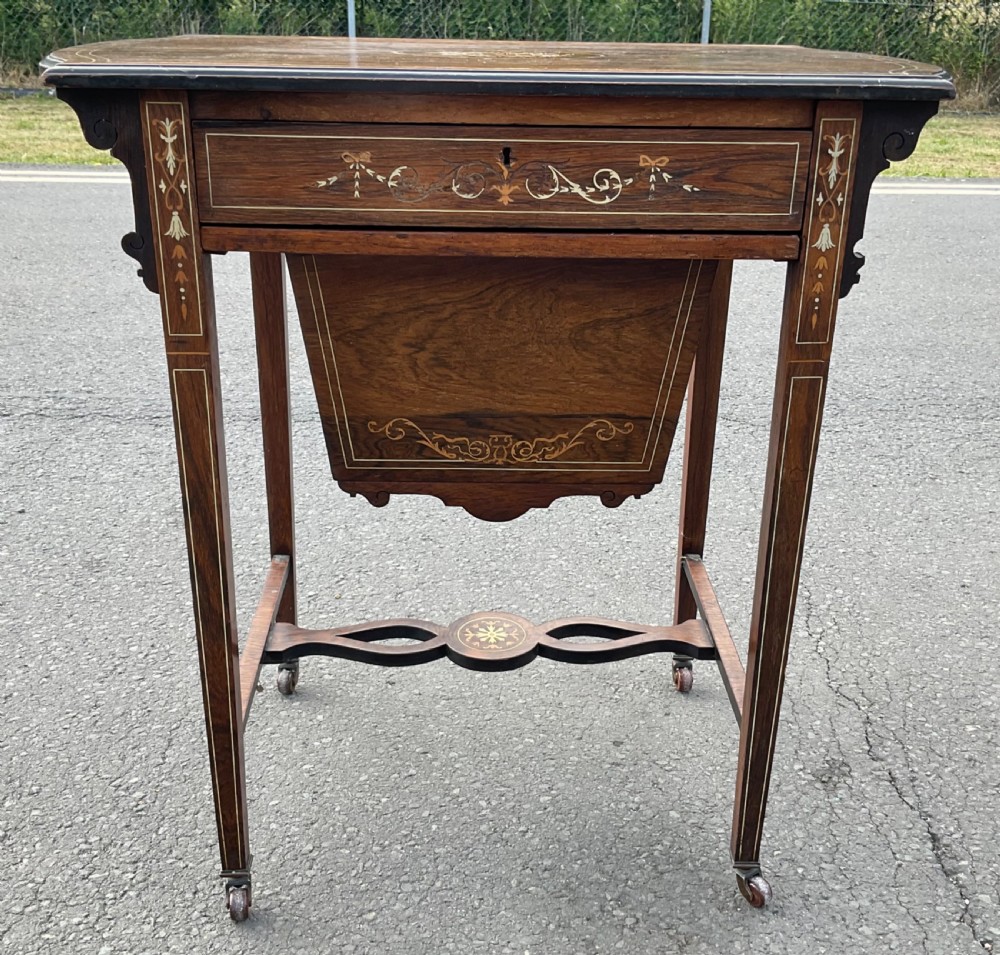 An Edwardian mahogany ladies work table featuring intricate floral marquetry inlay, a single drawer above a tapered well, slender square legs, and brass castors.