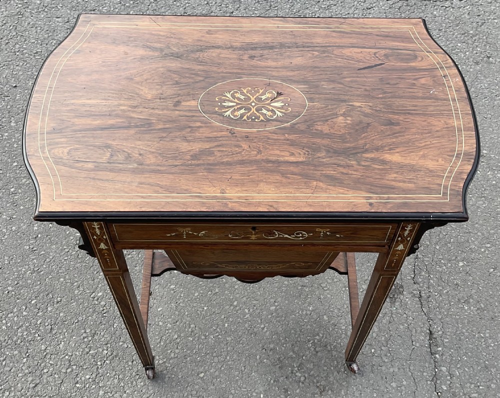 An Edwardian mahogany ladies work table featuring intricate floral marquetry inlay, a single drawer above a tapered well, slender square legs, and brass castors. View III