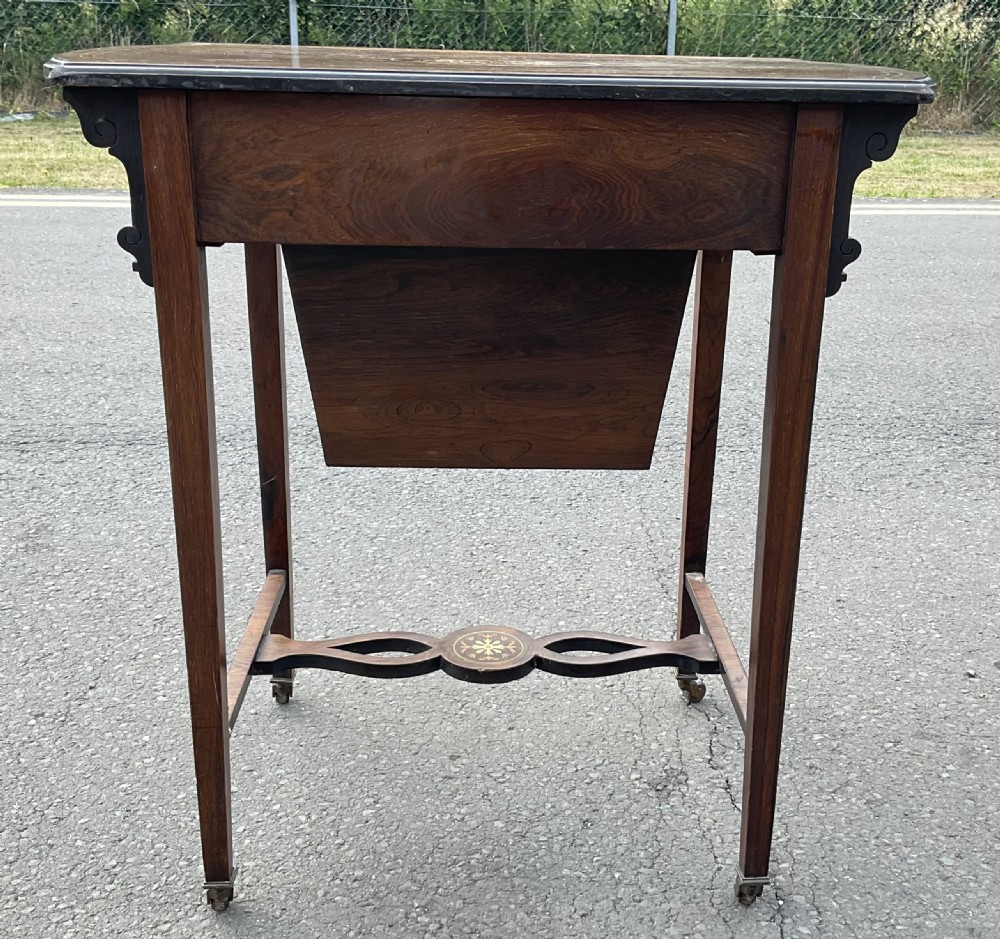 An Edwardian mahogany ladies work table featuring intricate floral marquetry inlay, a single drawer above a tapered well, slender square legs, and brass castors. View V