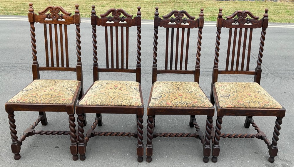 A set of four dark oak Jacobean style dining chairs featuring barley twist uprights, carved crest rails, and tapestry fabric seats.