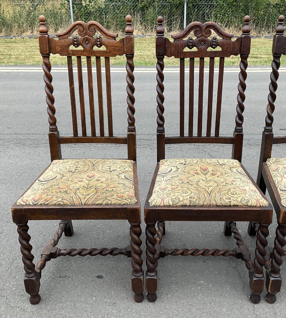 A set of four dark oak Jacobean style dining chairs featuring barley twist uprights, carved crest rails, and tapestry fabric seats. View VI