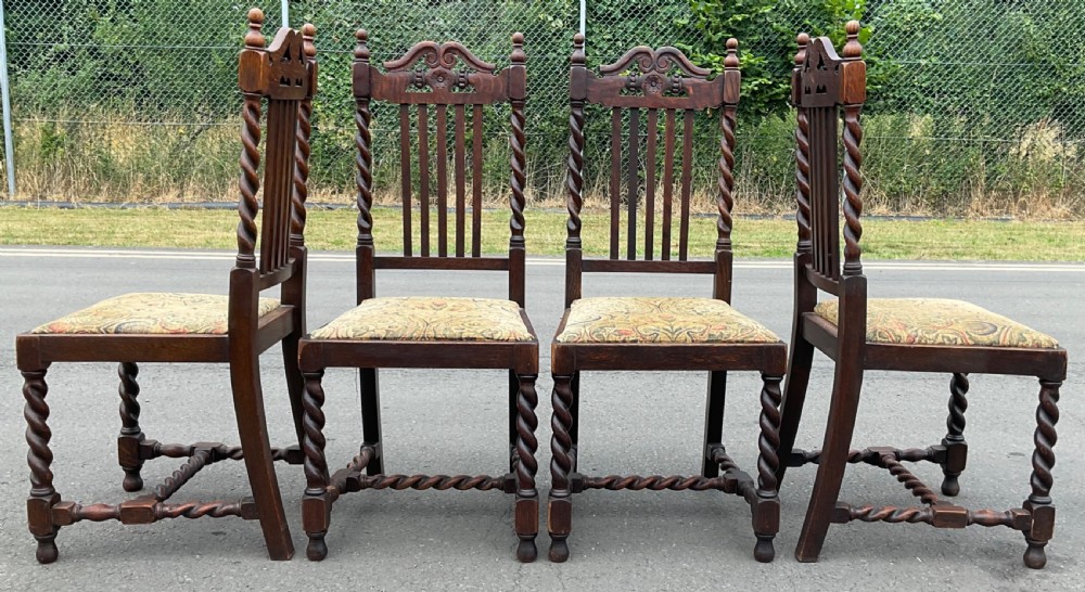 A set of four dark oak Jacobean style dining chairs featuring barley twist uprights, carved crest rails, and tapestry fabric seats. View VII