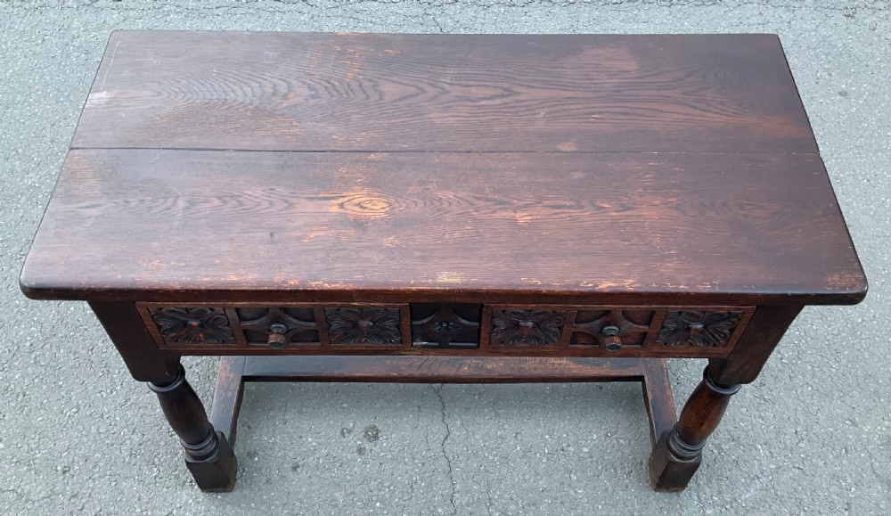 A dark brown oak writing table featuring two carved panel drawers, turned front legs, and an H-stretcher base. View VI
