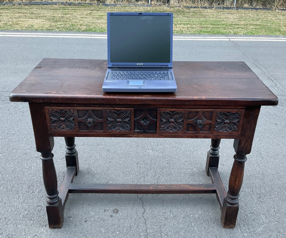 A dark brown oak writing table featuring two carved panel drawers, turned front legs, and an H-stretcher base. View VII