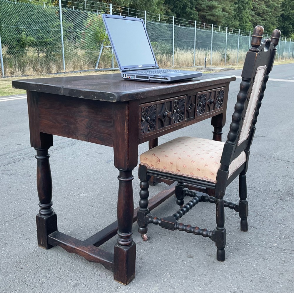 A dark brown oak writing table featuring two carved panel drawers, turned front legs, and an H-stretcher base. View VIII