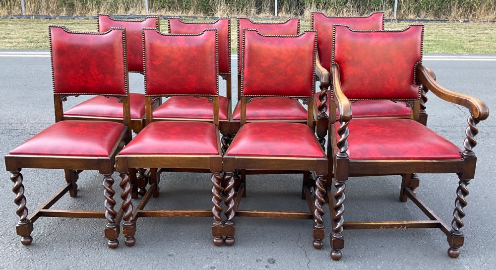 A set of eight oak dining chairs featuring red leather upholstery with brass stud detailing and spiral barley twist legs.