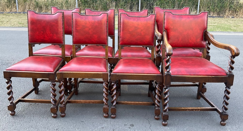 A set of eight oak dining chairs featuring red leather upholstery with brass stud detailing and spiral barley twist legs. View V