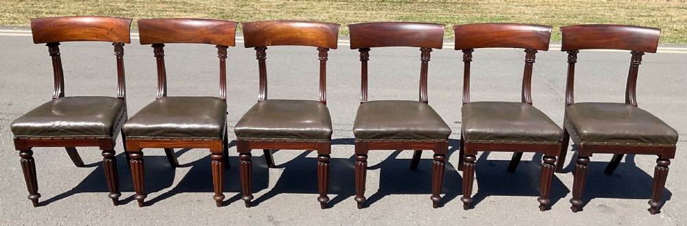 A set of six William IV mahogany dining chairs featuring curved top rails, reeded front legs, and dark green leather upholstered seats.
