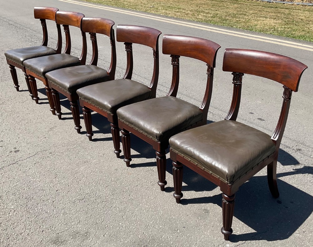A set of six William IV mahogany dining chairs featuring curved top rails, reeded front legs, and dark green leather upholstered seats. View IV