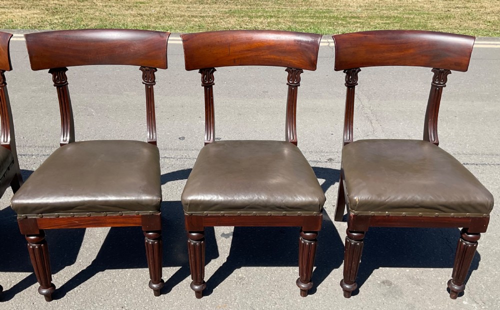 A set of six William IV mahogany dining chairs featuring curved top rails, reeded front legs, and dark green leather upholstered seats. View VI