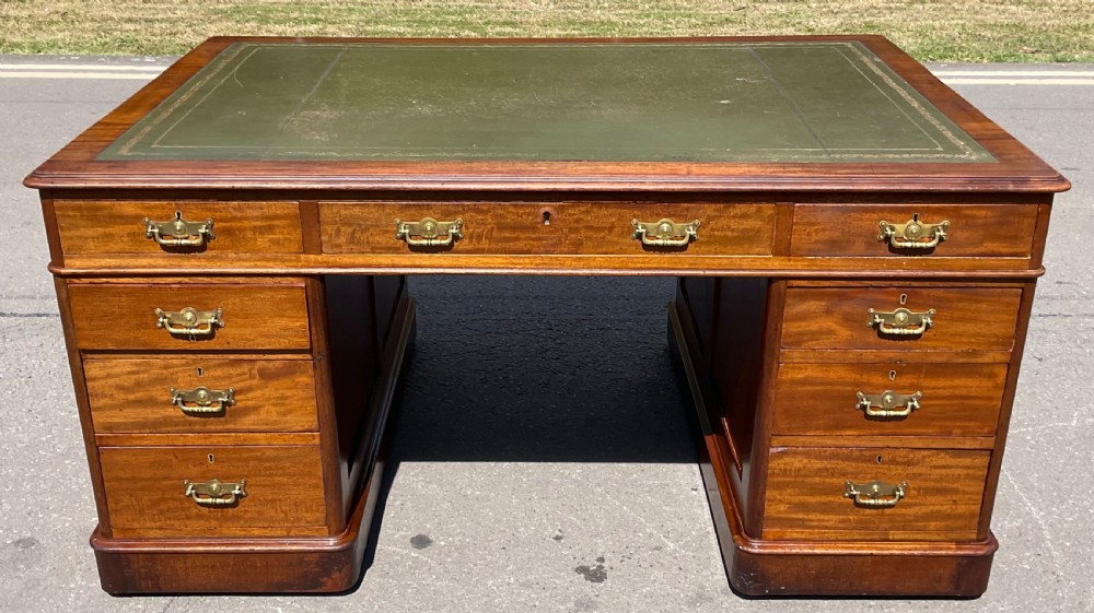 A Victorian mahogany pedestal desk featuring a green leather inset writing surface, nine drawers with brass handles, and twin pedestal bases.