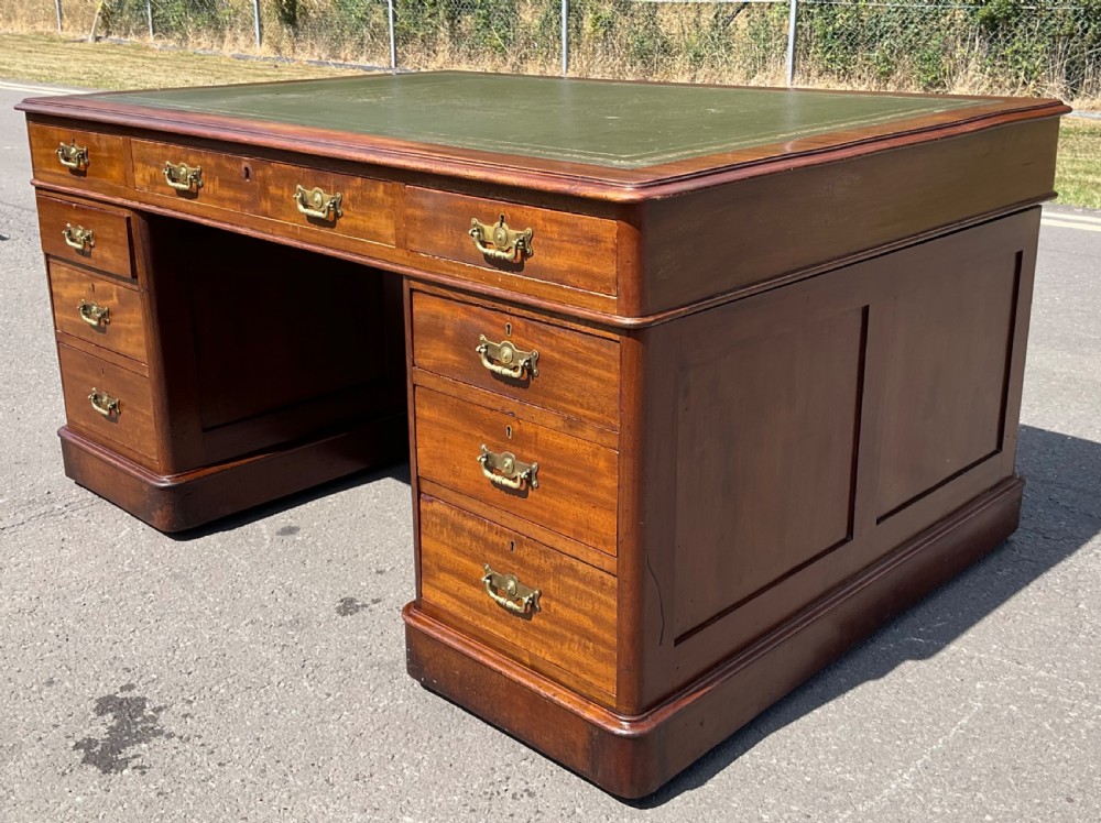 A Victorian mahogany pedestal desk featuring a green leather inset writing surface, nine drawers with brass handles, and twin pedestal bases. View IV