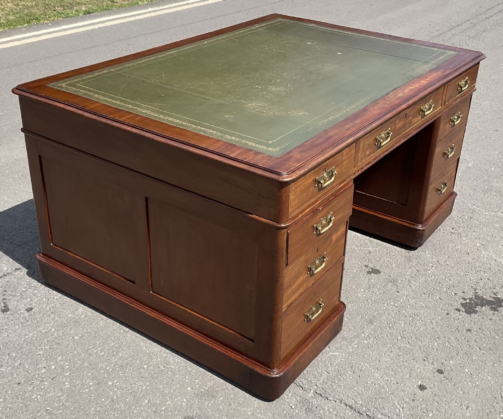 A Victorian mahogany pedestal desk featuring a green leather inset writing surface, nine drawers with brass handles, and twin pedestal bases. View V