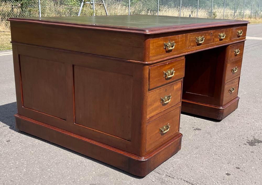 A Victorian mahogany pedestal desk featuring a green leather inset writing surface, nine drawers with brass handles, and twin pedestal bases. View VI